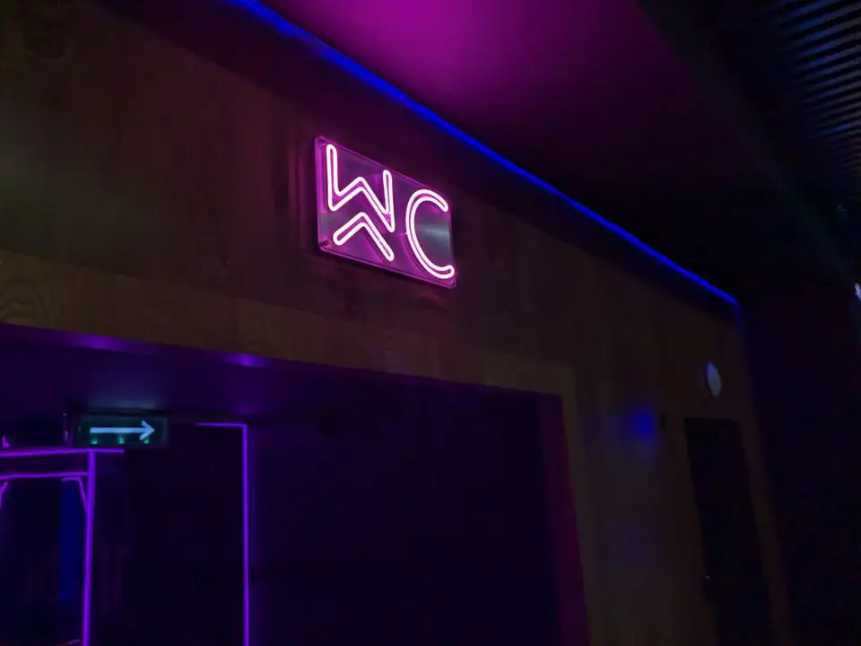 Розовый неоновый указатель WC над проходом в тёмном помещении